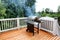 Barbecue grill cooking with visual smoke in open outdoor deck during summer day