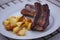 Barbecued Sticky Ribs and pork chops from grill with oven baked potatoes on a plate with wooden background