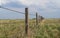 Barbed wire fence with blue cloudy skies bordering farm property in the prairies wild grass of alberta