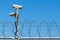 Barbed wire fence with security camera on blue sky