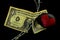 Barbed wire running through a old weathered and ripped dollar bill and a black stone with a painted red heart laying on it