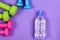 Barbells in pink, green and blue colors near water bottle,