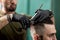 Barber in black gloves cuts with scissors hair of stylish man at a barbershop