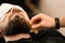 Barber combs beard with comb while shaving Caucasian man