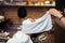 Barber covers the face of a man with a hot towel. Traditional ritual of shaving the beard with hot and cold compresses in a old