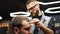 Barber in glasses cuts bearded man`s hair with a clipper in barbershop. Hipster hairstyling and hair cutting in salon