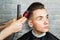 Barber hair styling of young guy in the barbershop on brick wall background, hairdresser makes hairstyle for a young man.