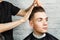 Barber hair styling of young guy in the barbershop on brick wall background, hairdresser makes hairstyle for a young man.