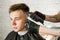 Barber hand in gloves cut hair and shaves young man on a brick wall background. Close up portrait of a guy