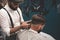 Barber man shaves client in barbershop. Stylish barber makes haircut for guy