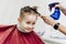 Barber`s hands spray the little boy`s hair with a spray gun