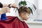 Barber`s hands spray the little boy`s hair with a spray gun