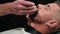 Barber shaves the client\'s beard on a chair. Beard haircut. Barber to shave a beard with an electric razor. Grooming of