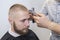 Barber shaves the client`s head using electric trimmer and comb, selective focus