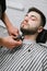 Barber shaves an electric beaver shaver in a barber shop chair. Male percussionist does hairstyle to client, holds trimmer in