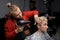 Barber stylish man with a Caucasian beard blow-drying hair for a guy client in the process of cutting in a salon or barbershop