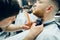 Barber trimming bearded man with shaving machine in barbershop. Hairstyling process. Close-up of a Hairstylist cutting