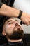 A barber trims a Caucasian clients mustache with a trimmer.