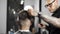 Barber wets hair by spray and combs them, tattoed barber makes haircut for customer at the barber shop, man`s haircut