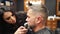 Barber woman cuts man`s beard with a trimmer in barbershop. Men`s hairstyling and hair cutting in salon. Grooming the