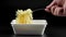 bare caucasian hand with fork stirring freshly cooked instant noodle in styrofoam bowl on black background in slow