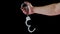 bare caucasian hand holding opened silver steel handcuffs on black background