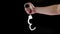 bare caucasian hand holding opened silver steel handcuffs on black background