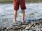 Bare feet of an unspecified boy in the water on the coast with stone beach