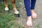 Bare feet of young girl standing near horse hooves close up outdoors