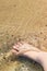 Bare foot of a woman in the clean and transparent sea water with yellow sand and sea stones