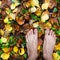 Bare man feet stands on colored autumn foliage in the right bottom corner of square frame, top view, copy space