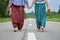 Barefoot adult woman and a young girl hand in hand walking along the asphalt road