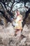 A barefoot blonde woman in a yellow summer dress is reading a book in the shade of olive trees on a beautiful sunny day