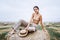 Barefoot brunette in linen pants and bare shoulders sitting on a hay bales in warm autumn day. Woman looking at camera. Behind her