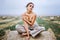 Barefoot brunette in linen pants and bare shoulders sitting on a hay bales in warm autumn day. Woman looking at camera. Behind her