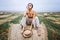 Barefoot brunette in linen pants and bare shoulders sitting on a hay bales in warm autumn day. Woman looking at camera. Behind her