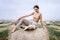 Barefoot brunette in linen pants and bare shoulders sitting on a hay bales in warm autumn day. Woman looking at camera. Behind her