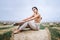 Barefoot brunette in linen pants and bare shoulders sitting on a hay bales in warm autumn day. Woman looking at camera. Behind her