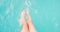 Barefoot female sunbathing playing feet in pure water at outdoor swimming pool