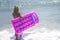 Barefoot girl in blue bikini at the sea. Slim tall girl in swimwear walking in the sea with pink inflatable pool raft