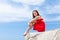 Barefoot girl sitting on rock against sky