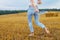 Barefoot girl with sneakers in hand walking in the agricultural field with haystack and bales
