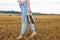Barefoot girl with sneakers in hand walking in the agricultural field with haystack and bales