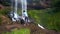 Barefoot guy with backpack climbs up stone by waterfall