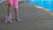 Barefoot legs of a little girl in pink shorts skating on a skateboard along the swimming pool