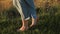 Barefoot legs of young woman walking in tall grass at summer