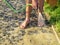 A barefoot worker washes sand from a newly laid granite stones with a garden hose with a rain. Stage of laying paving slabs.