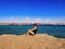 Barefoot young woman with blond braided hair sits on a rock against the background of the sea panorama of Sharm El Sheikh Egypt