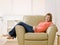 Barefoot young woman lounging on armchair at home