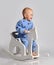 Barefooted baby boy in blue fleece jumpsuit with stars plays has fun riding white kids rocking horse toy swinging